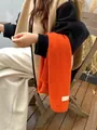 Detailopname van een feloranje gebreide wintersjaal met een wit merklabel erop - 160cm / Oranje