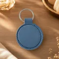 Minimalist blue circular PU leather keychain with silver ring on wooden desk background - Blue