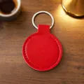 Premium minimalist red circular PU leather keychain with silver ring on a rustic wooden desk - Red