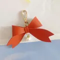 Detailed close-up of a red PU leather bow keychain with gold clasp and pearl charm. - Tangerine