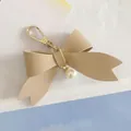 Close-up of a beige PU leather bowknot keychain with a pearl charm and gold clasp. - Khaki