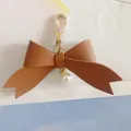 Detail view of brown PU leather bow keychain with elegant faux pearl charm. - Brown
