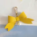 Detailed close-up view of a vibrant yellow PU leather bow keychain with a pearl charm. - Yellow