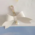 Détail macro d'un porte-clés nœud en cuir PU blanc avec fermoir doré et pendentif perle - Blanc