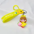 Close-up detail of a cute yellow silicone keychain featuring a cartoon girl holding a pink peach - Yellow