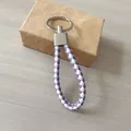 Primer plano de un llavero de cuero trenzado morado y blanco sobre una caja de regalo. - Blanco y Púrpura