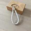 Llavero de cuero trenzado blanco y plata con caja de regalo sobre fondo de madera - Blanco