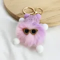 Detailed close-up of a cute purple plush monster keychain wearing stylish gold sunglasses. - Size 3