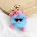 Close-up of a cute blue fluffy monster keychain with pink hat and sunglasses accessory. - Size 6
