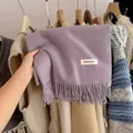 Close-up of a soft purple knitted scarf with tassels and a minimalist brand label. - Grey Purple