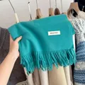 Detail view of a thick blue knitted winter scarf with fringes and a decorative label. - Lake Blue