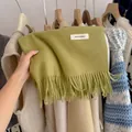 Macro view of a soft lime green knitted scarf with tassels and white brand label - 194cm / Olive Green