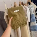 Detailed view of olive green solid color knitted scarf featuring decorative tassels and label - 194cm / Korean Style Green