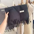 Close-up of a thick dark grey knit scarf featuring fringe details and a white brand tag. - 194cm / Black Series