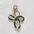 Handmade multicolor crochet bow keychain with pearl pendant on white fabric background - Gradient Green