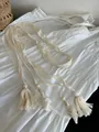 Detailweergave van handgemaakte crème macramé riem met kwastjes op witte jurk - Kanten Kwastjesstijl