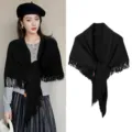 Detail view of a black knitted triangular shawl featuring elegant fringe and tag - Black