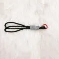 Hand-woven black and grey paracord keychain with red metal ring on soft white faux fur background - Black