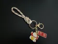Handmade woven wrist rope keychain featuring lucky cat charm and red blessing tag pendant - Khaki