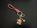 Pink hand-woven rope keychain with gold-plated Maneki-neko charm on black background - Pink