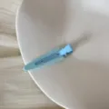 Détail en gros plan d'une pince à cheveux triangulaire bleu clair sur assiette - Clip Triangulaire Sans Trace (FJ83071) / Bleu