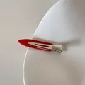 Détail macro d'une pince à cheveux en acétate rouge avec fermoir argenté et texte blanc - Rouge