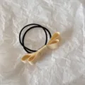 Detailed close-up view of a minimalist cream fabric bow hair tie on a white textured background - Deep Yellow