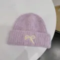 Detail of a purple fuzzy beanie with an ivory embroidered bow on the folded cuff. - One Size / Purple