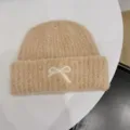 Detailed macro view of the white bow embroidery on a beige fuzzy knit winter beanie hat - One Size / Camel