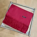 Detalle de una bufanda de cachemira roja premium con flecos en un soporte moderno - 180cm / Burdeos
