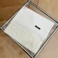 Vista detallada de una bufanda de cachemira crema con flecos sobre mesa de cristal - 180cm / Blanco