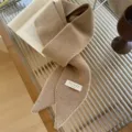 Primer plano de una bufanda de punto camel con una etiqueta de marca 'Trendy' en un escritorio - 185x8cm / Camel Arroz
