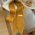 Detalle de primer plano de una bufanda de punto estrecha amarillo mostaza con etiqueta - 185x8cm / Amarillo jengibre