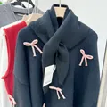 Close-up of black wool blend knitted scarf with cute pink bow accents. - Black