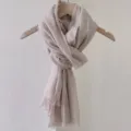 Detail view of a beige cotton-linen scarf with fringed edges on a wooden hanger. - 180cm / Camel