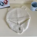 Close-up detail of soft white knitted beanie featuring cute bear ears and protective ear flaps - White