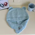 Macro detail of a light blue knitted winter hat featuring cute bear ears and a silver heart pin - Melange Blue