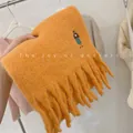 Close-up of thick orange wool blend scarf featuring cute girl embroidery and long tassels - Embroidered Girl / Orange