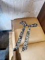 Gedetailleerd overzicht van een zijden lint met zebraprint in een strik op een lederen stoel - 140cm / Zwart Zebra