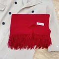 Soft warm red winter scarf with fringe tassels and minimalist tag, folded on a beige wool coat - Burgundy