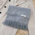 Soft grey winter scarf with elegant tassel detail laid over a beige wool coat background - Light Heather Grey