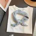 Pañuelo cuadrado con flores azules anudado sobre una camiseta blanca - Flor Azul