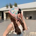Model wearing a pink floral cotton linen small square headscarf in a sunny outdoor cafe. - Lotus Root Pink Small Flower