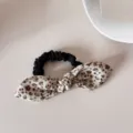 Detailed view of a vintage floral bow scrunchie with delicate blue and brown patterns. - Scrunchie (Beige Floral Bow)