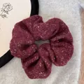 Close-up of a burgundy felt scrunchie with gold sparkles on a fuzzy background. - Red Gold Silk Scrunchie