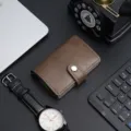 Brown PU leather pop-up card holder with aluminum shell and button clasp on a desk - Coffee