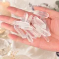 Nahaufnahme einer Hand, die natürliche klare Bergkristallsäulen hält mit Transparenz - 100g (3-5cm)
