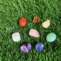 Seven colorful tumbled natural crystals scattered on artificial green grass background - Approx 20-25mm / Set of 8