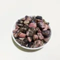 Natural pink and black Rhodonite tumbled stones displayed in a small white bowl - Rhodonite / 100g Pack