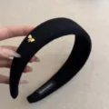 Detalle de diadema de fieltro negro con dije de lazo dorado y etiqueta artesanal - Negro